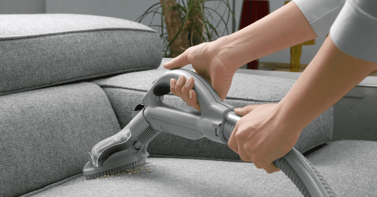 A woman cleaning a couch with a vacuum cleaner